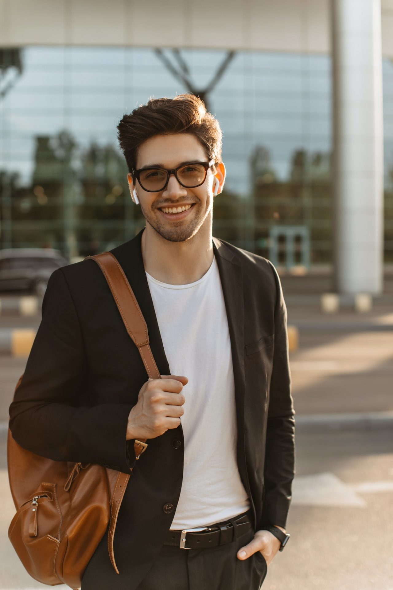 Happy businessman in eyeglasses looks into camera and smiles sincerely. Brunette guy in black jacke
